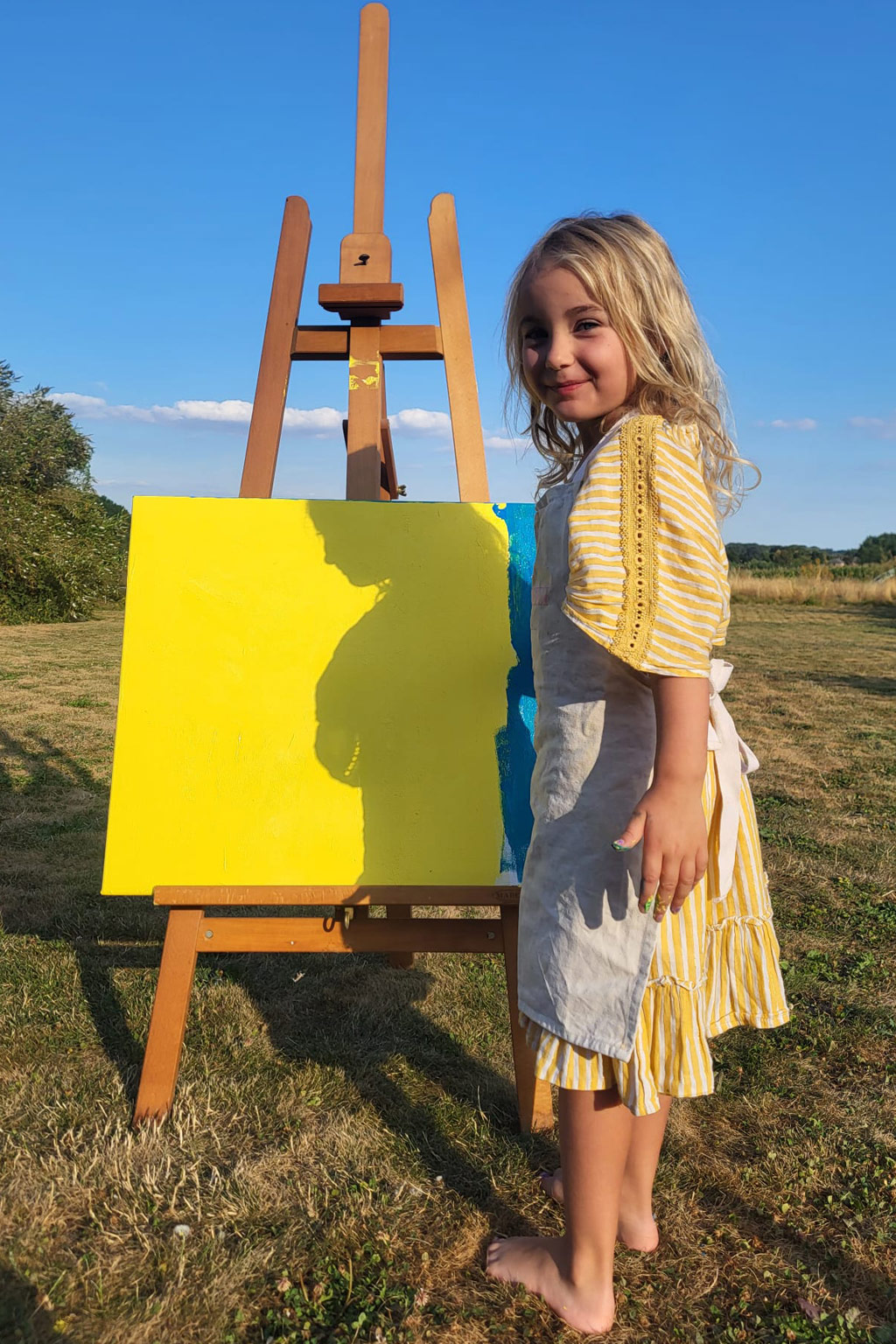 Une enfant devant son tableau peint, sur un chevalet en plein air